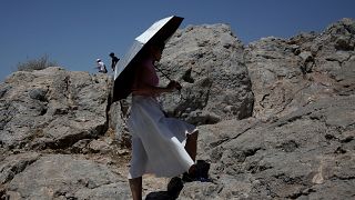 Τουρίστρια κρατάει ομπρέλα ενώ ανεβαίνει στον βράχο του Αρείου Πάγου