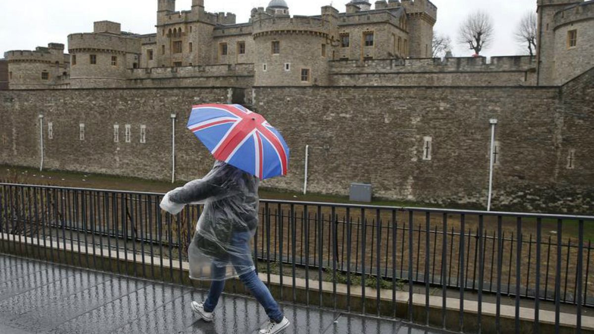 عابری با چتر منقش به پرچم بریتانیا از کنار برج لندن می گذرد