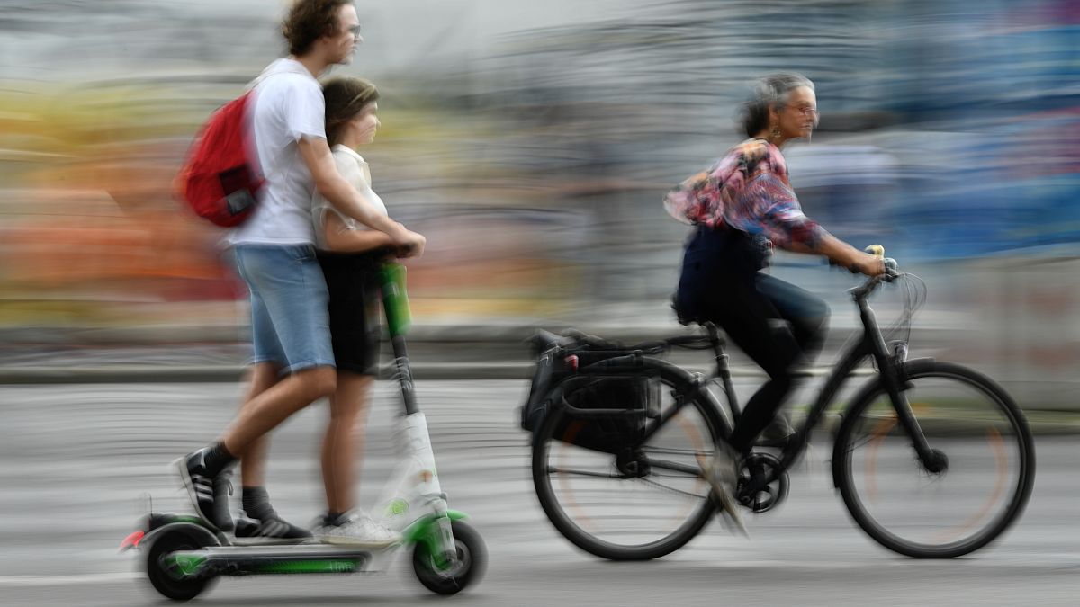 Radfahrerin überholt in Berlin zwei Verkehrsteilnehmer auf einem E-Tretroller.