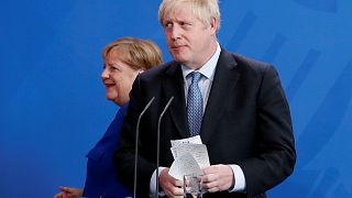 El Primer Ministro de Gran Bretaña, Boris Johnson, sostiene sus notas mientras asiste a una conferencia de prensa con la Canciller alemana Angela Merkel.