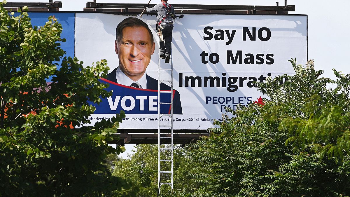 عامل يزيل لوحة إعلانات كبيرة مناهضة للهجرة عليها صورة لماكسيم بارنيه زعيم الحزب الشعبي الكندي اليميني في تورونتو