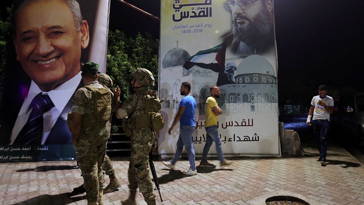 جنود لبنانيون بالقرب من ملصق عليه صورة أمين عام حزب الله، حسن نصر الله، على الحدود الجنوبية اللبنانية 