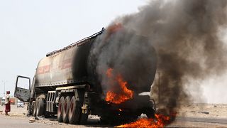 رجل يقف بجانب شاحنة صهريج نفط اشتعلت فيها النيران خلال اشتباكات بين الانفصاليين والقوات الحكومية بالقرب من عدن