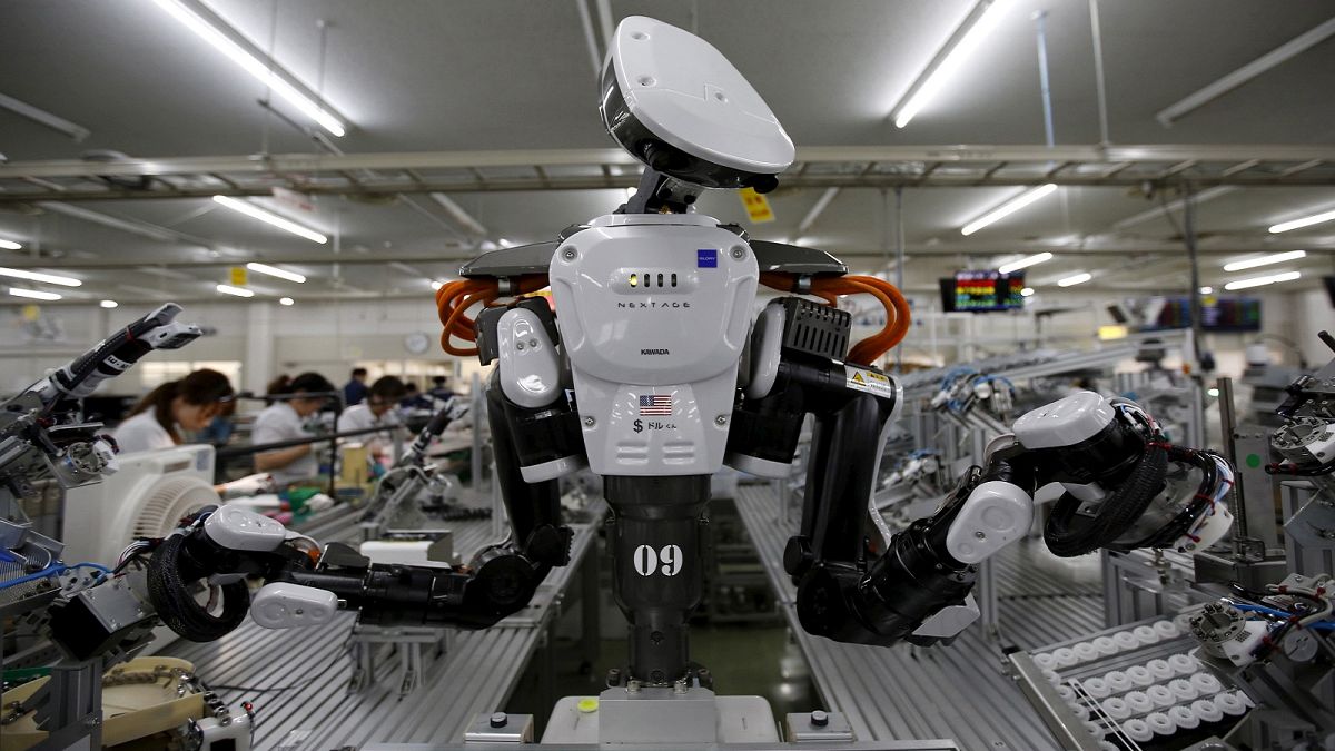 A humanoid robot works side by side with employees at a factory of Glory Ltd., a manufacturer of automatic change dispensers, in Kazo, north of Tokyo