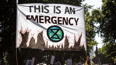 A banner declaring climate emergency alongside an Extinction Rebellion symbol is held high above the crowd A banner declaring climate emergency alongside an Extinction Rebellion symbol is held high above the crowd