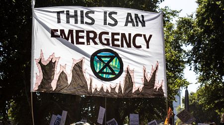 A banner declaring climate emergency alongside an Extinction Rebellion symbol is held high above the crowd