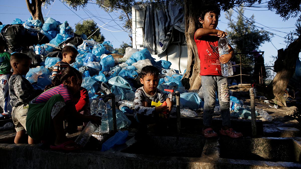 Children fill bottles with water next to a pile of garbage on the island of Lesbos