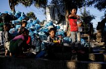 طفال يملئون الزجاجات بالمياه بجانب كومة من القمامة في مخيم مؤقت للاجئين والمهاجرين في جزيرة ليسبوس باليونان