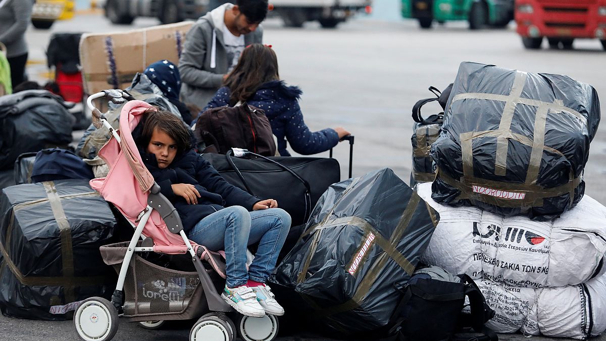 فتاة تجلس في عربة أطفال بينما ينتظر اللاجئون والمهاجرون نقلهم إلى مخيمات في ميناء بيرايوس في اليونان