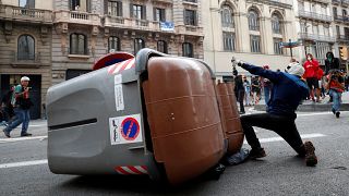 Gewalttätiger Demonstrant in Barcelona neben umgestürzten Müllcontainern.