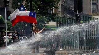 المتظاهرون يلوحون بالأعلام التشيلية بينما تقوم قوات الأمن برشهم بخراطيم المياه أثناء الاحتجاج على النموذج الاقتصادي للدولة في تشيلي في سانتياغو، 23 أكتوبر / تشرين الأول 2019
