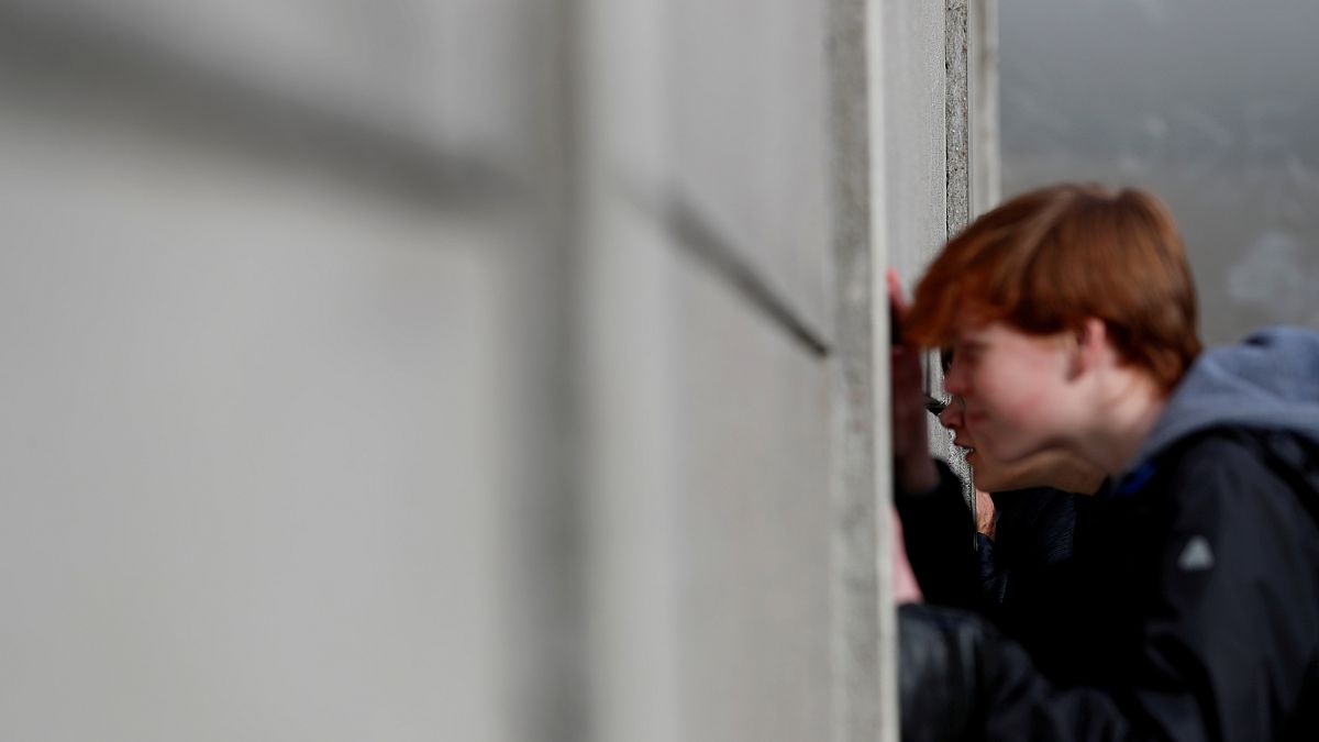 Visitors peers through segments of Wall at the Berlin Wall memorial on Bernauer Strasse in Berlin