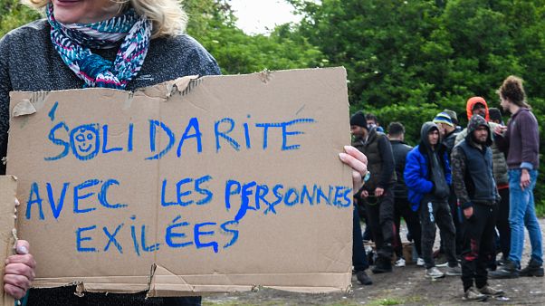 A woman holds a sign reading "Solidarity with people in exile" as she takes part in a solidarity march in support of migrants, in Calais, northern France on May 8, 2019. A woman holds a sign reading "Solidarity with people in exile" as she takes part in a solidarity march in support of migrants, in Calais, northern France on May 8, 2019.