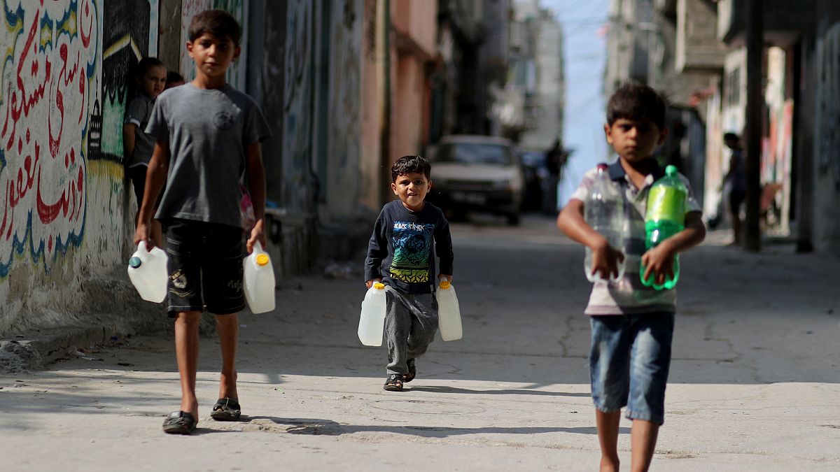 فتيان فلسطينيون يحملون زجاجات مياه أثناء سيرهم في مخيم الشاطئ في مدينة غزة