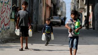 فتيان فلسطينيون يحملون زجاجات مياه أثناء سيرهم في مخيم الشاطئ في مدينة غزة