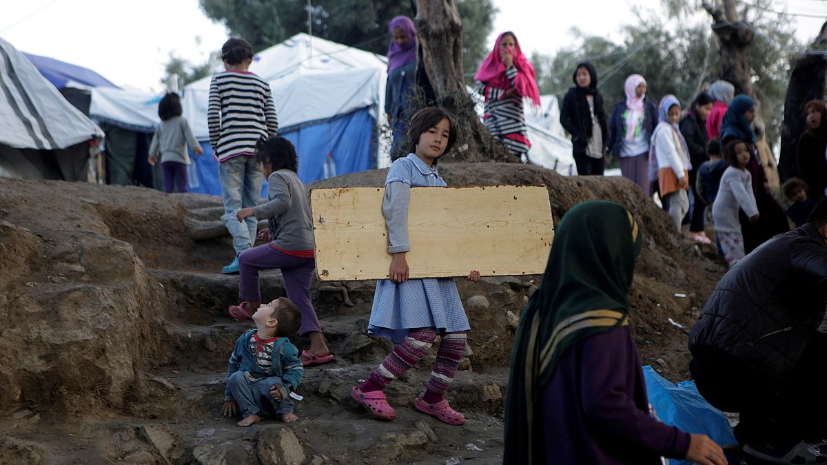 فتاة تحمل لوحًا خشبيًا في مخيم مؤقت للاجئين والمهاجرين في جزيرة ليسبوس باليونان