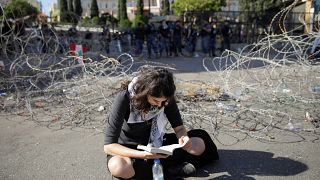 متظاهرة تقرأ كتاباً وهي تجلس بجوار الأسلاك الشائكة خلال الاحتجاجات المستمرة المناهضة للحكومة في بيروت