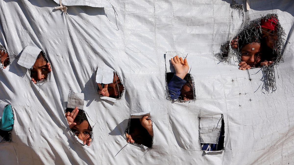 Gyerekek kukucskálnak ki egy sátor lyukain keresztül a szíriai Al-hol táborban