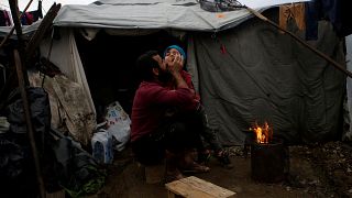 لاجئ سوري يعانق ابنه بالقرب من خيمة للجوء في اليونان