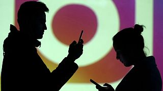 Silhouettes of mobile users are seen next to a screen projection of Instagram logo