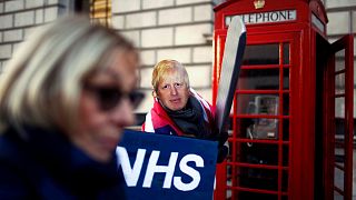 A healthcare professional dressed as Britain's Prime Minister Johnson attends a demonstration demanding NHS public service must remain protected from commercial exploitation