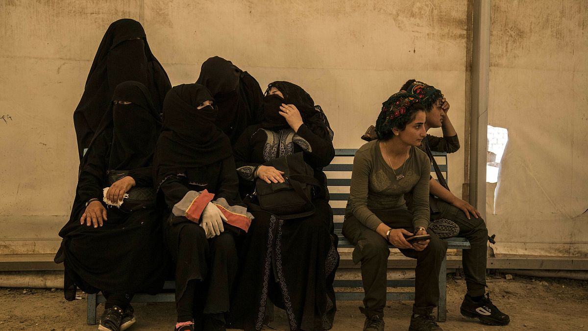 نساء مرتبطات بمقاتلي جماعة الدولة الإسلامية يجلسن بجانب حارسات من قوات سوريا الديمقراطية في مخيم الهول يونيو 2019