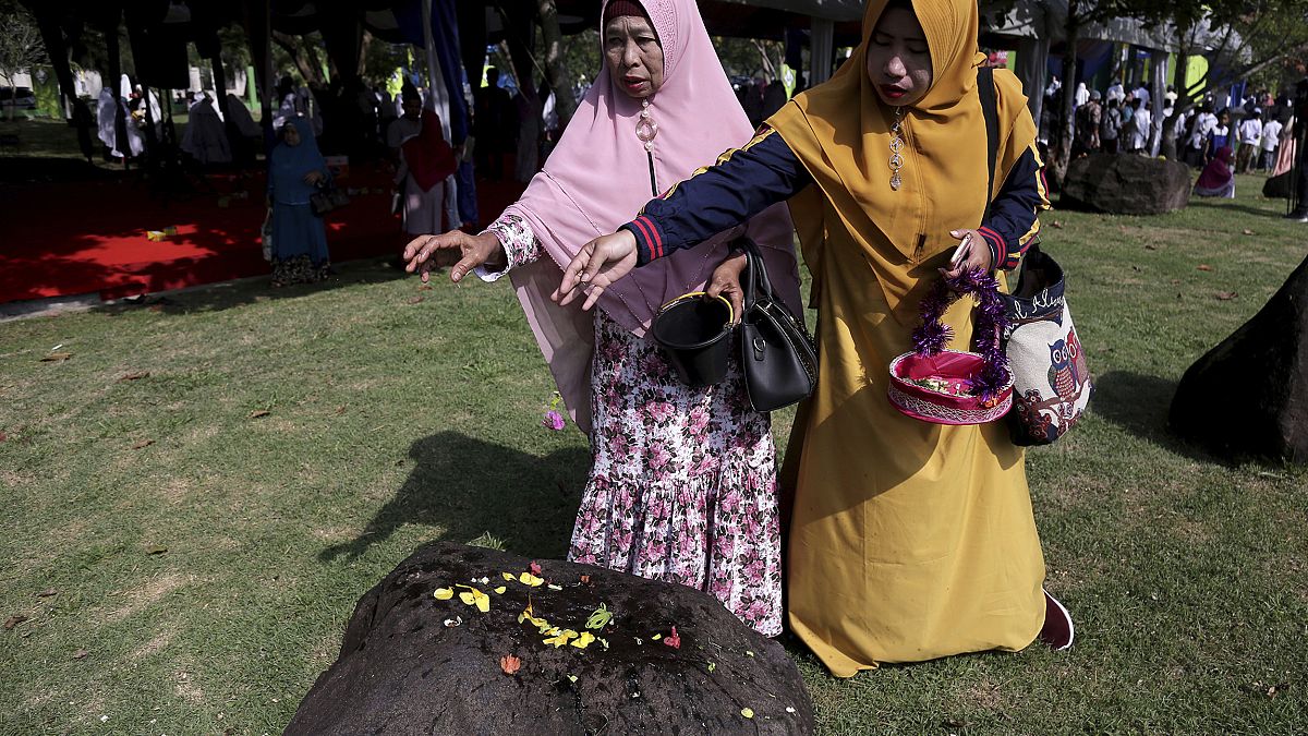Women sprinkle flowers on a stone marking the mass grave for the victims of 2004 tsunami, during a commemorative service in Banda Aceh, Indonesia, Dec. 26, 2018. 