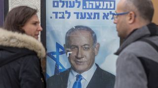People look at a poster of Israel's Prime minister and governing Likud party leader Benjamin Netanyahu.