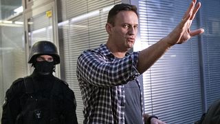 Alexei Navalny gestures while speaking to the media as a security officer guards an entrance of the Foundation for Fighting Corruption office in Moscow, Russia,  Dec.26