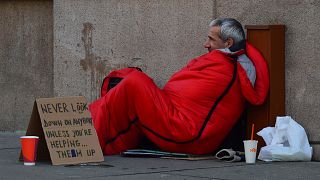 Obdachloser mit einem Schild "Schau nie auf jemanden herab, es sei denn, du hilfst ihm, aufzustehen"