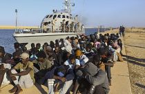 مهاجرون تم إنقاذهم يجلسون قرب قارب تابع لخفر السواحل في مدينة خومس، ليبيا، 1 أكتوبر 2019