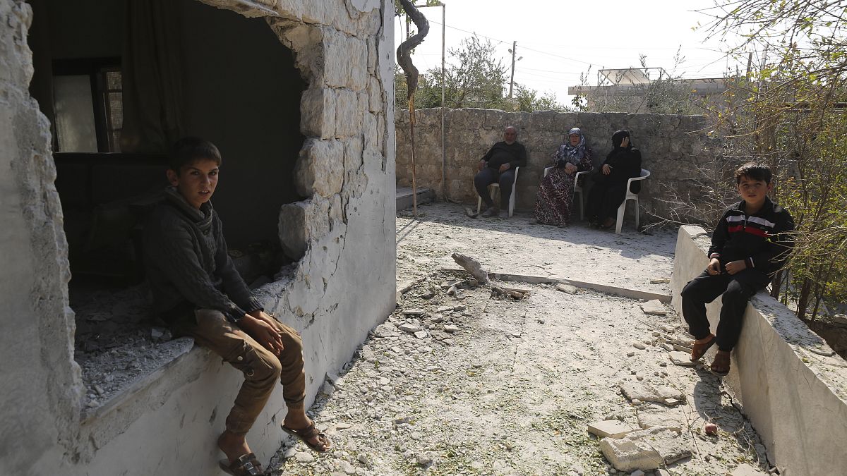طفال يجلسون بجوار منزلهم المدمر في قرية بريشا في محافظة إدلب، سوريا 2019