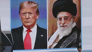 A man walks by a huge screen showing U.S. President Donald Trump, left, and Iranian Supreme Leader Ayatollah Ali Khamenei