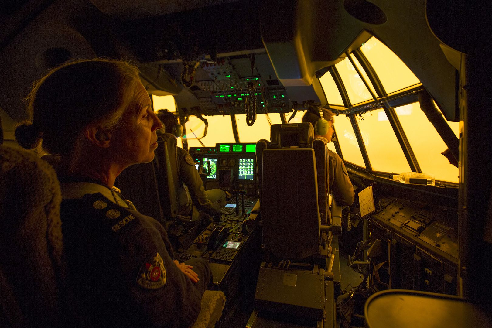 A New South Wales Fire and Rescue station officer looks out the window of a C-130J Hercules aircraft as a warm glow from wildfires near Coffs Harbour seen through the window.