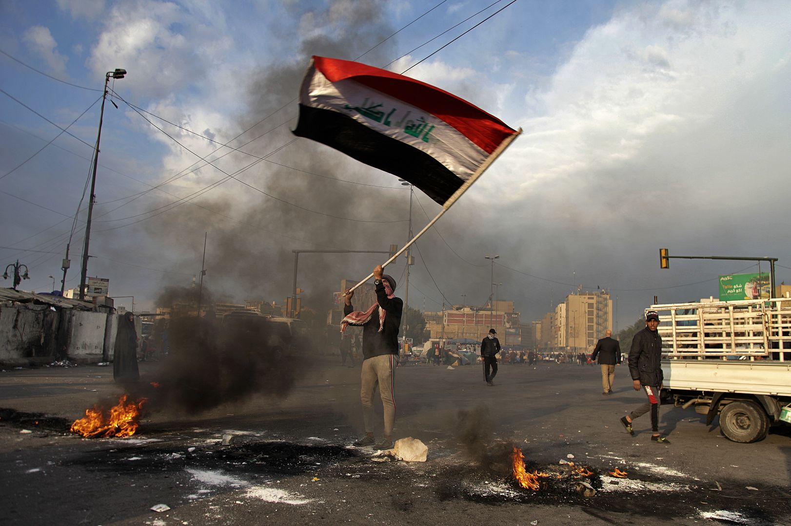 A protester waves the national flag while demonstrators set fire to close streets near Tahrir Square during a demonstration against the Iranian missile strike in Baghdad, Iraq