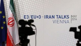 Cameras stand in front of flags from the EU and Iran and poster of the Iran talks