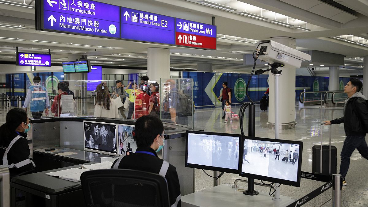 مسؤول مراقبة الصحة يقوم باستخدام الماسح الضوئي لدرجة الحرارة للمسافرين في مطار هونغ كونغ