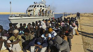 مهاجرون تم إنقاذهم يجلسون قرب قارب تابع لخفر السواحل في مدينة خومس، ليبيا، 1 أكتوبر 2019