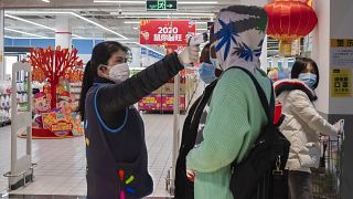 A worker takes the temperature of a customer at the entrance of a Walmart store in Wuhan in central China's Hubei Province