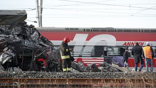 The wreckage of the locomotive of a high-speed train crammed onto another train on adjacent tracks, as the rest of train is seen in the background, after it derailed. Italy.