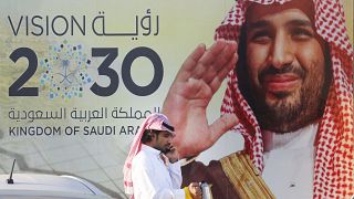 سعودي بجانب لافتة تظهر "رؤية 2030"، التي أطلقها محمد بن سلمان 05/02/2020