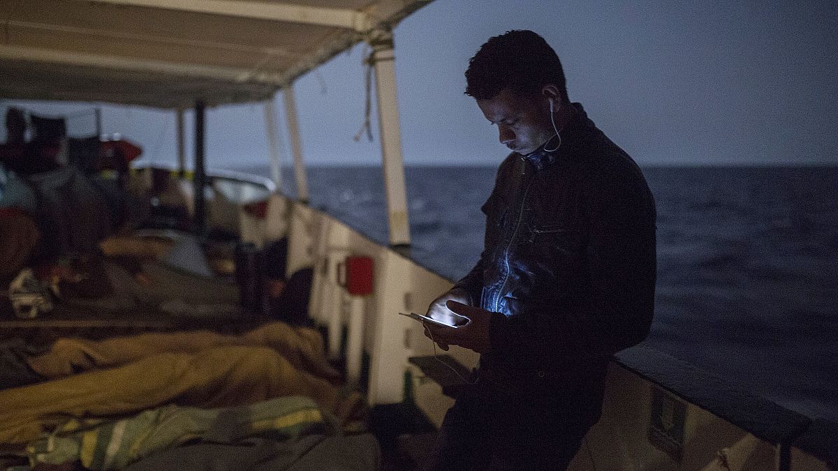 A migrant checks is cellular phone as other sleep on the deck of the Open Arms aid boat, of Proactiva Open Arms Spanish NGO, Sunday, July 1, 2018.