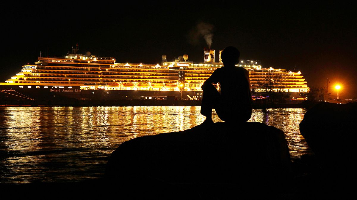 رجل يرقب السفينة التي تملكها "هولاند أمريكا لاين"، وهي راسية في ميناء سيهانوكفيل صباح الجمعة، قبيل هبوط مئات المسافرين منها.