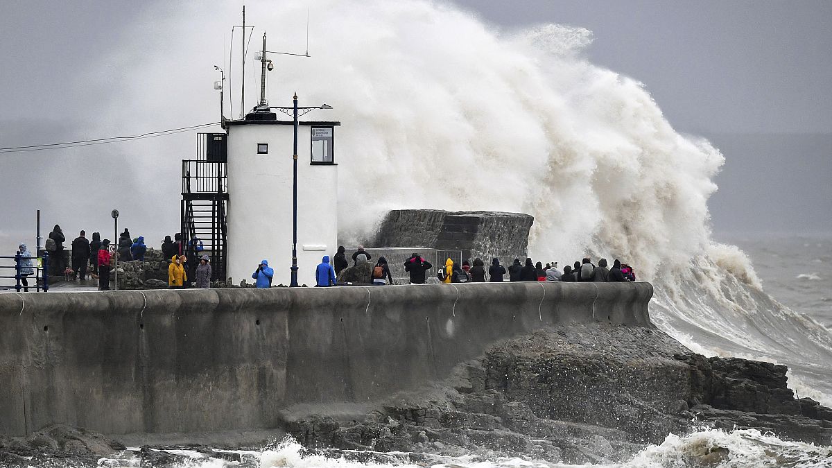 People watch waves and rough seas pound against the harbour wall at Porthcawl, Wales