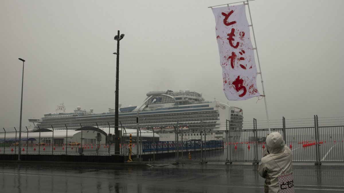 رجل يلوح  بلافتة مكتوب عليها "أصدقاء" باليابانية بالقرب من سفينة دايموند برنسيس