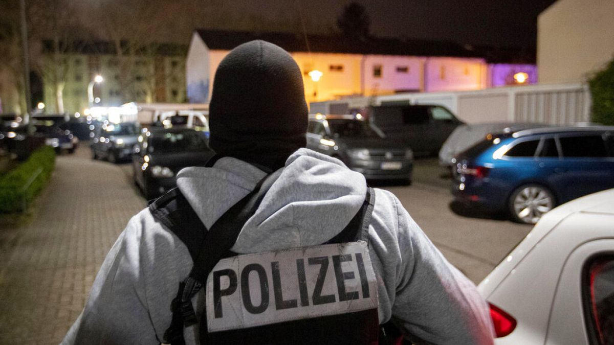 A police officer guards the road in front of a house that is searched through by police in Hanau, Germany Thursday, Feb. 20, 2020. (AP Photo/Michael Probst)