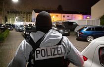 A police officer guards the road in front of a house that is searched through by police in Hanau, Germany Thursday, Feb. 20, 2020. (AP Photo/Michael Probst)