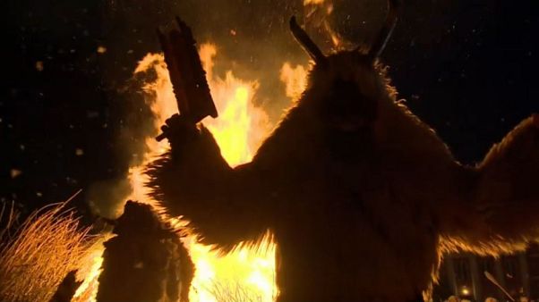 Creature in sheepskin cloak watches coffin representing winter burn Creature in sheepskin cloak watches coffin representing winter burn
