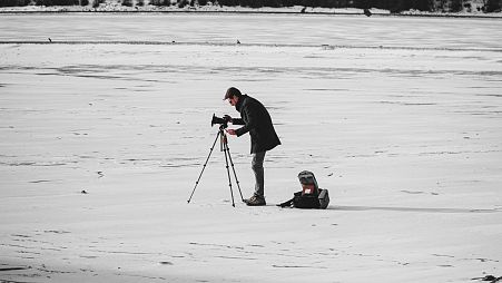 A man filming on a snowy backdrop.