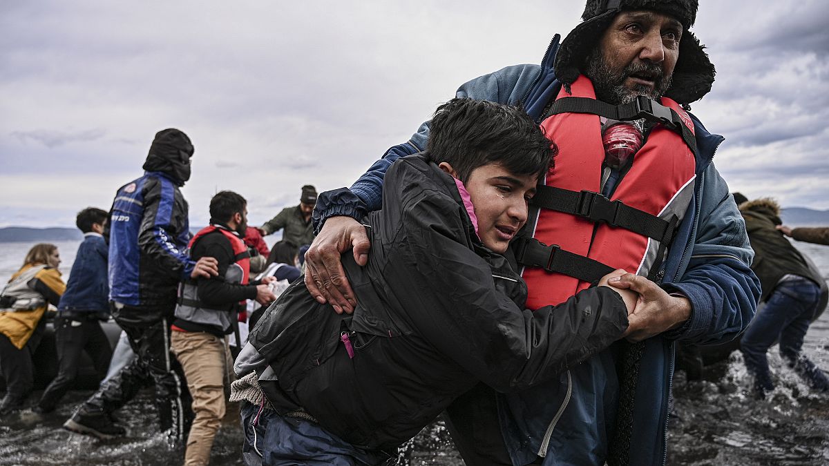 A man helps a young boy to walk after a dinghy with 54 Afghan refugees landed ashore the Greek island of Lesbos 